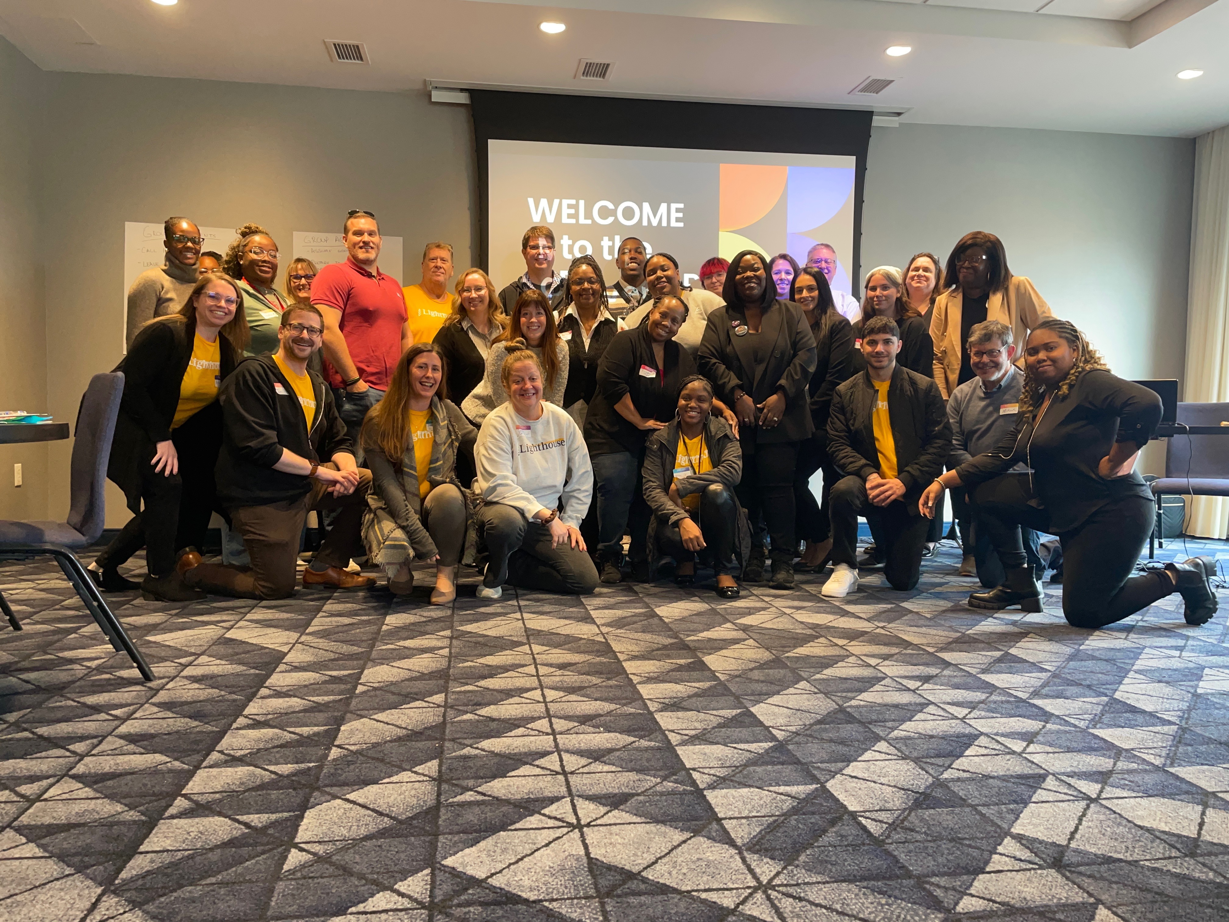 Large group of advocates and staff gathered together in front of a welcome screen at a community training event